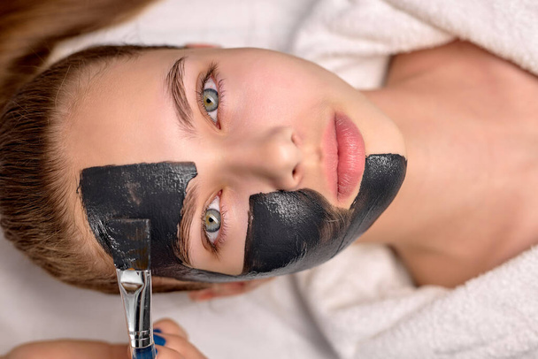 Procedure for applying black mask on face of beautiful woman, top view. Spa treatments - Photo, image