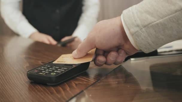 Slowmo zbliżenie nierozpoznawalny człowiek dołączanie karty kredytowej do terminala do dokonywania płatności zbliżeniowych w recepcji hotelu - Materiał filmowy, wideo