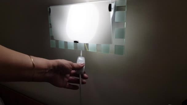 Ženská ruka zapíná a vypíná noční lampu zavěšenou na stěně, 4k video - Záběry, video