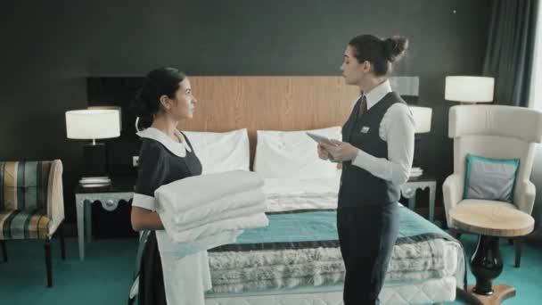 Medium shot της γυναίκας διευθυντής του ξενοδοχείου με ψηφιακό tablet δωμάτιο ελέγχου πριν από τους επισκέπτες check-in, λέει οικονόμος κρατώντας λευκά λινά για να κάνει το κρεβάτι - Πλάνα, βίντεο