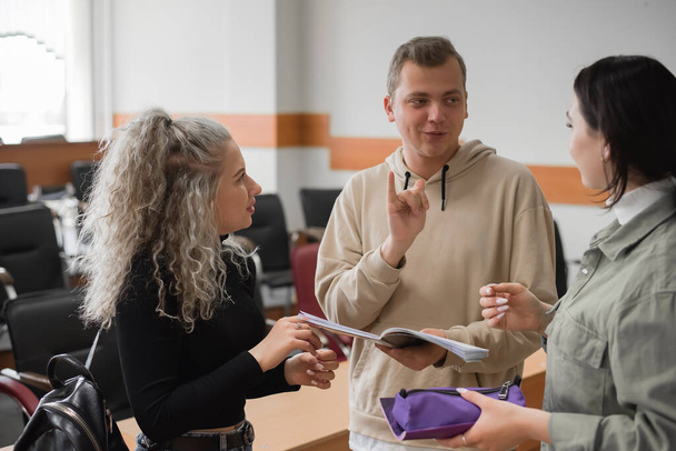Two girls and a guy are talking in sign language. Three deaf students chatting in a university classroom. - Foto, Bild