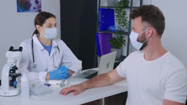 γιατρός μετρά τη θερμοκρασία του ασθενούς με θερμόμετρο μη επαφής κατά τη διάρκεια του ραντεβού στην κλινική - Πλάνα, βίντεο