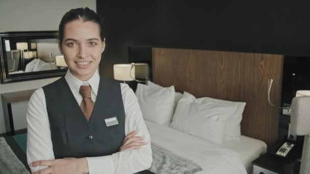 Średni powolny portret atrakcyjnej młodej kierowniczki hotelu uśmiechniętej do aparatu stojącej z rękami złożonymi w luksusowym pokoju hotelowym - Materiał filmowy, wideo