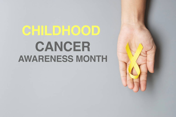 Childhood Cancer Awareness month, hand holding Gold Yellow Ribbon for supporting people living and illness. children Healthcare and World cancer day concept - Photo, Image