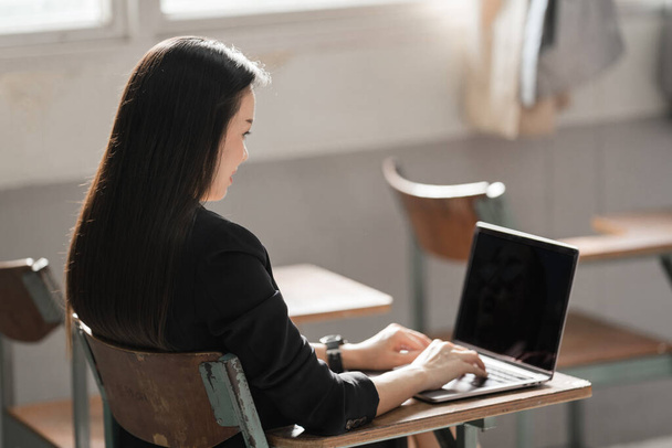 Zdjęcie Stockowy portret pewnej siebie Azjatki nauczycielki w czarnym garniturze służbowym mundur z tabletem cyfrowym i laptopem uczyć nowoczesnego języka w klasie - Zdjęcie, obraz