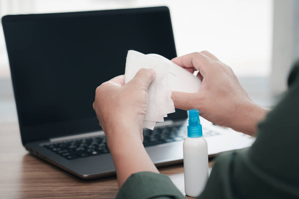 Cerca de la mano de un hombre de limpieza y desinfección del espacio de trabajo. Desinfectar toallitas para limpiar la superficie del escritorio, portátil, ratón en la oficina. Detener la propagación - Foto, imagen