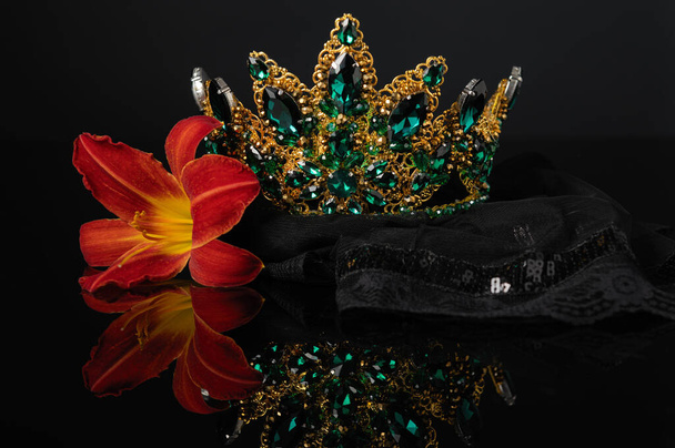 beautiful crown, feminine head ornament with green stones and a lily flower on a black background with reflection - Photo, Image