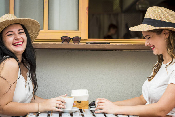 Paar junger und glücklicher kaukasischer Mädchen haben gemeinsam Spaß beim Lachen und Kaffeepause an der Bar im Freien - fröhliche Frauen in Freundschaft oder Beziehung genießen Freizeit - Foto, Bild