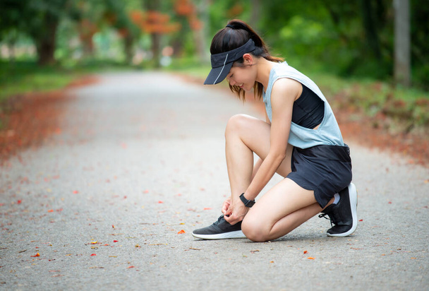 Portrait of young runner woman knee down on the road for tying shoelaces. Conceptual of woman getting ready for jogging in the park. - Photo, Image