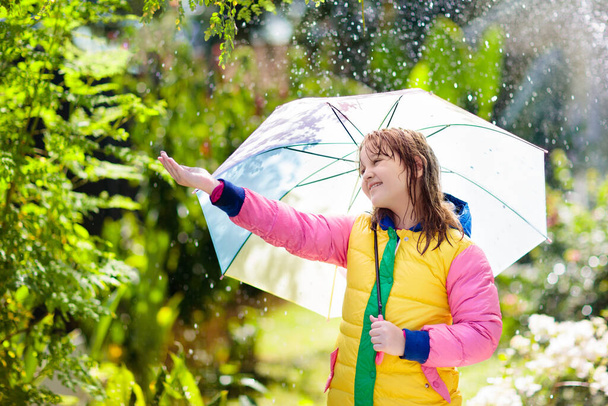 Lapsi leikkii syksyllä sateessa. Poika sateenvarjon kanssa. Pikkutyttö juoksee puistossa syksyllä. Ulkona hauskaa lapsille säästä riippumatta. Sade vedenpitävä kulumista, saappaat ja takki lapsille. - Valokuva, kuva