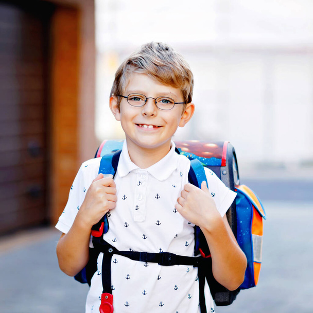 Χαρούμενο αγοράκι με γυαλιά και σακίδιο ή τσάντα. Μαθητής στο δρόμο για το σχολείο. Πορτρέτο του υγιούς αξιολάτρευτο παιδί σε εξωτερικούς χώρους. Μαθητής, μαθητής, πίσω στο σχολείο. Ηλικία δημοτικού σχολείου - Φωτογραφία, εικόνα