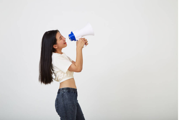 cheerful young Asian woman holding megaphone  announcement in isolated studio - Fotó, kép
