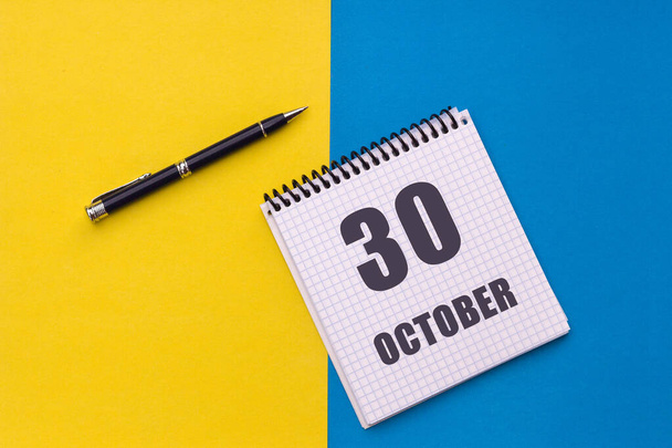 30. Oktober. Tag 30 des Monats, Kalenderdatum. Notizbuch mit Spirale und Stift liegt auf gelb-blauem Hintergrund. - Foto, Bild