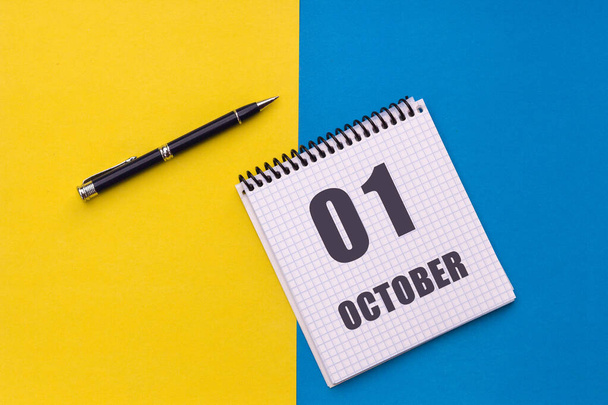 October 1st. Day 1 of month, calendar date. Notebook with a spiral and pen lies on a yellow-blue background. - Photo, Image
