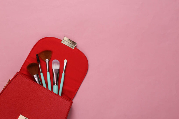 Pembe arka planda makyaj fırçası olan kırmızı çanta. Üst Manzara. Boşluğu kopyala - Fotoğraf, Görsel