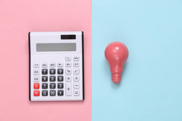 Calculator and pink light bulb on pinj blue background. Top view. Minimalism - Foto, Imagen