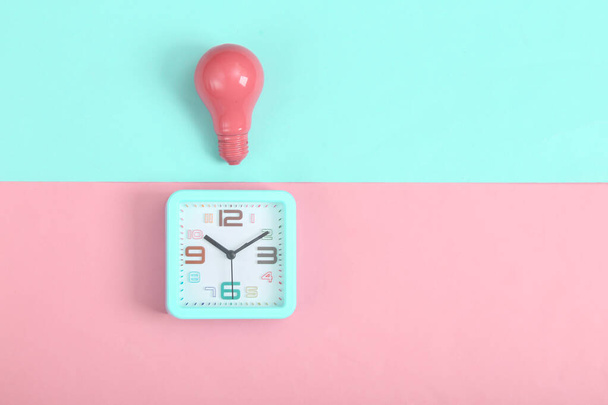 Poplašné hodiny a růžová žárovka na růžovém modrém pozadí. Minimalismus. Horní pohled - Fotografie, Obrázek