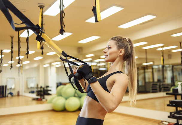 Mujer joven en forma entrena con cinturones de resistencia trx en el gimnasio de fitness. Estilo de vida saludable. Entrenamiento de peso corporal - Foto, Imagen