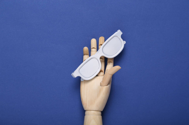 Wooden hand holding white glasses on blue background - Photo, Image