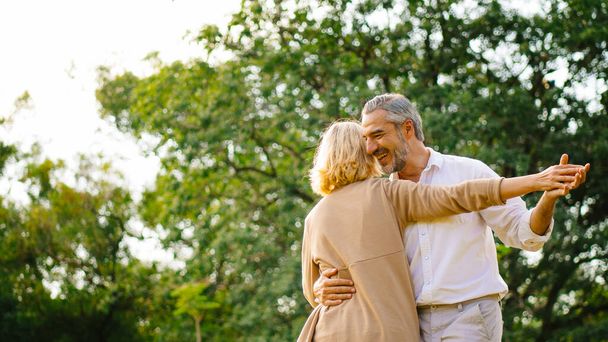 Senior elegant caucasian couple dancing looking at each other feeling love and cherish on their anniversary in the park with copy space, happily retired spouse, well-managed retirement life concept. - 写真・画像