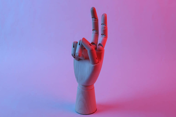 Wooden hand shows v gesture in pink blue gradient neon light - Fotó, kép