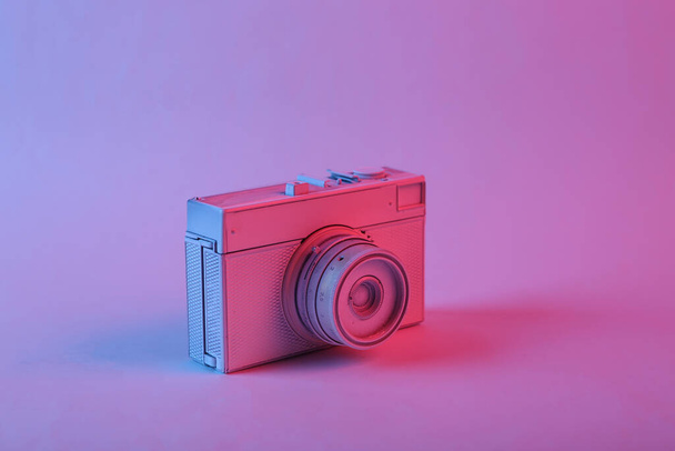 White camera in pink blue gradient neon light. Minimalism - Zdjęcie, obraz