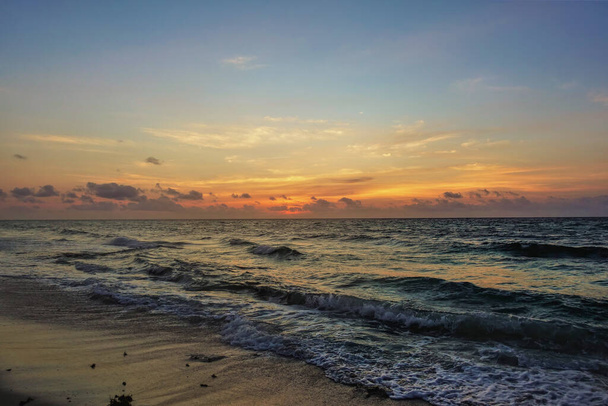 Aamunkoitto Karibianmeren yllä. Taivas horisontin yläpuolella on merkitty oranssilla. Surffausaallot vaahtoavat hiekkarannalla. Etelä-Korea  - Valokuva, kuva