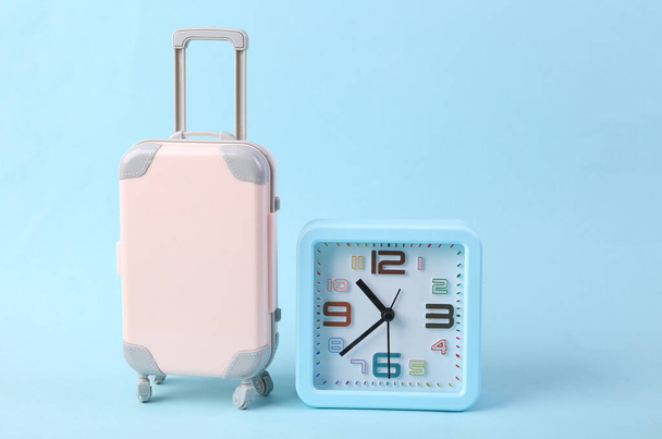 Travel time. Alarm clock and mini luggage model on blue background - Photo, Image