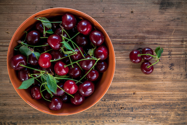 ripe cherries with leaves in bowl on old wooden rustic backgroun - Photo, Image