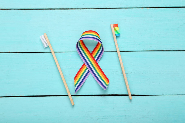 Due spazzolini da denti con simbolo lgbt nastro arcobaleno su sfondo blu in legno - Foto, immagini