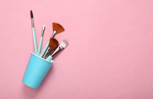 Makeup brushes in cardboard cup on pink pastel background - Фото, зображення