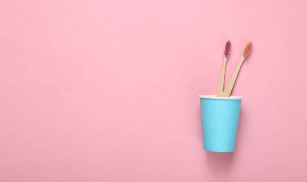 Dos cepillos de dientes de bambú ecológico en taza de cartón sobre fondo rosa - Foto, imagen