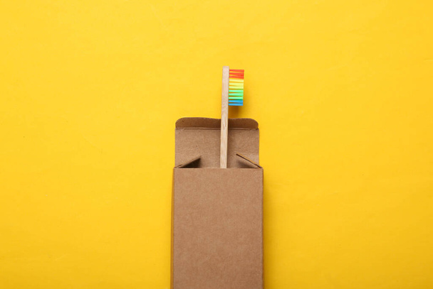 Радужная зубная щетка в картонной коробке на желтом фоне. - Фото, изображение