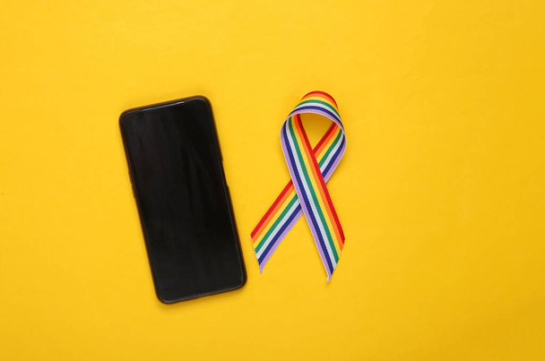 Fita LGBT arco-íris orgulho fita símbolo com smartphone no fundo amarelo. - Foto, Imagem