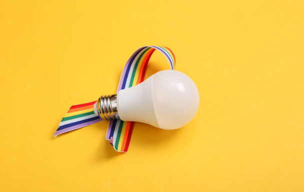 Glühbirne mit LGBT-Regenbogenband auf gelbem Hintergrund. - Foto, Bild