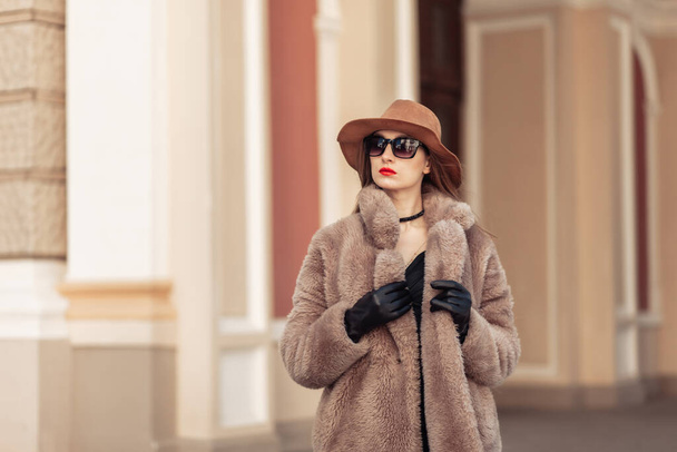 市内の明るい晴れた日に暖かい毛皮のコート、帽子、サングラスのファッション女性の肖像画 - 写真・画像