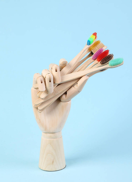 Деревянная рука держит зубные щетки на синем фоне - Фото, изображение