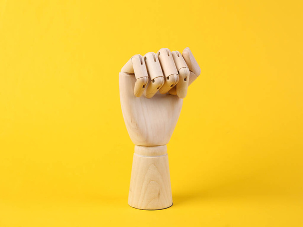 Ξύλινο χέρι δείχνει μια χειρονομία γροθιά σε ένα κίτρινο φόντο. Σύμβολο φεμινισμού - Φωτογραφία, εικόνα