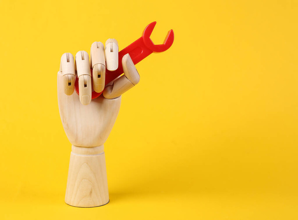Wooden hand holds toys wrench on yellow background - Foto, immagini