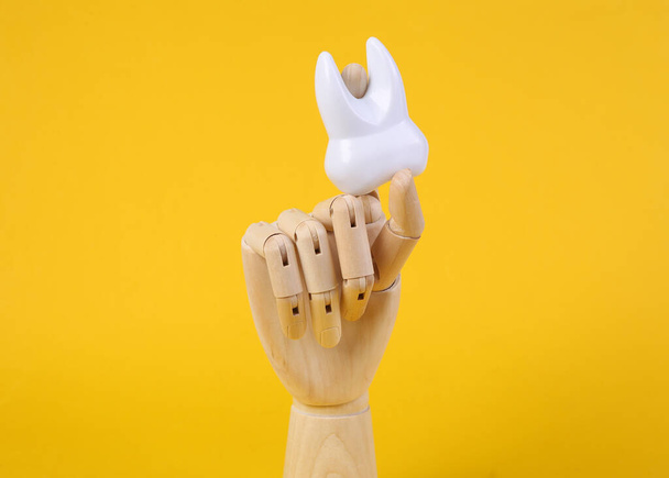 Wooden hand holds tooth on yellow background - Fotografie, Obrázek