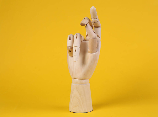 Деревянная рука щелкает пальцами на желтом фоне - Фото, изображение