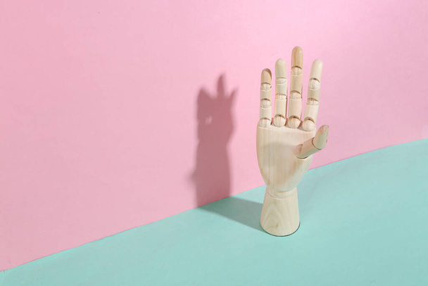 Ξύλινο χέρι σε μπλε ροζ παστέλ φόντο. Μοντέρνα σκιά. Αντίληψη τέχνης. Ελαχιστοποίηση - Φωτογραφία, εικόνα