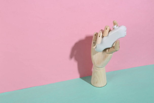 Mano de madera que sostiene el controlador moderno sobre fondo pastel rosa azul. Sombra de moda. Arte conceptual. Minimalismo. Diseño creativo - Foto, Imagen