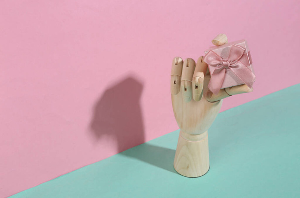 Деревянная рука с подарочной коробкой на голубом розовом пастельном фоне. Модная тень. Концептуальное искусство. Минимализм. Креативная планировка - Фото, изображение