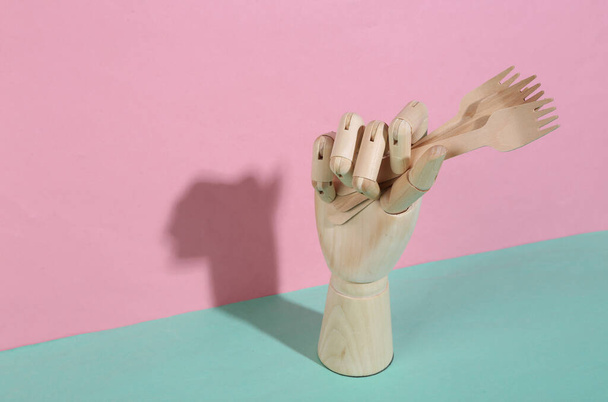 Drewniane ręce trzymające drewniane widelce na niebieskim różowym pastelowym tle. Modny cień. Sztuka koncepcyjna. Minimalizm. Kreatywny układ - Zdjęcie, obraz