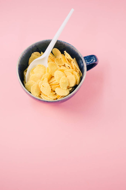A vertical shot of corn flakes on a cup with plastic spoon isolated on a pink background - Foto, afbeelding