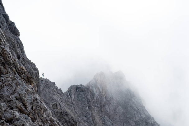 A person standing on a sharp rocky cliff on the Zugspitze peak with mist hiding everything around - Foto, immagini