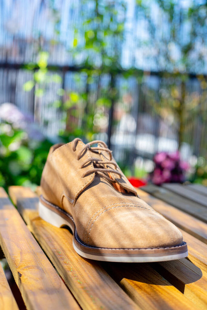 A vertical shot of a men's beige buck shoe on a wooden surface outdoors - Foto, Bild