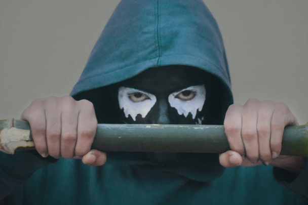 A young male with scary black and white skull face paint posing with a baseball bat - Foto, afbeelding