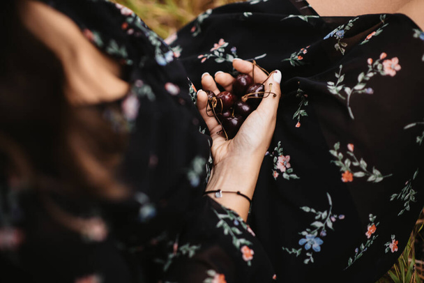 A selective focus shot of a woman wearing a dress and holding cherries - Foto, immagini